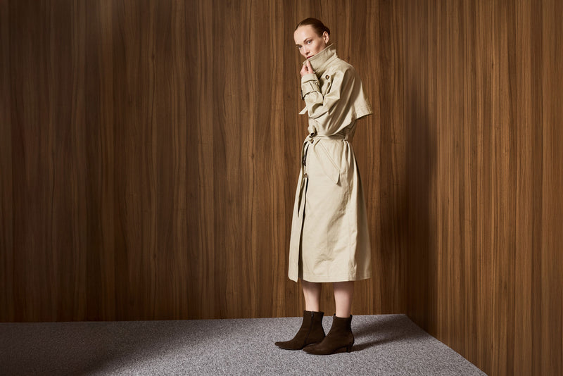 Woman in a beige trench coat standing against a wooden wall wearing the Celina boot by Paul Green.